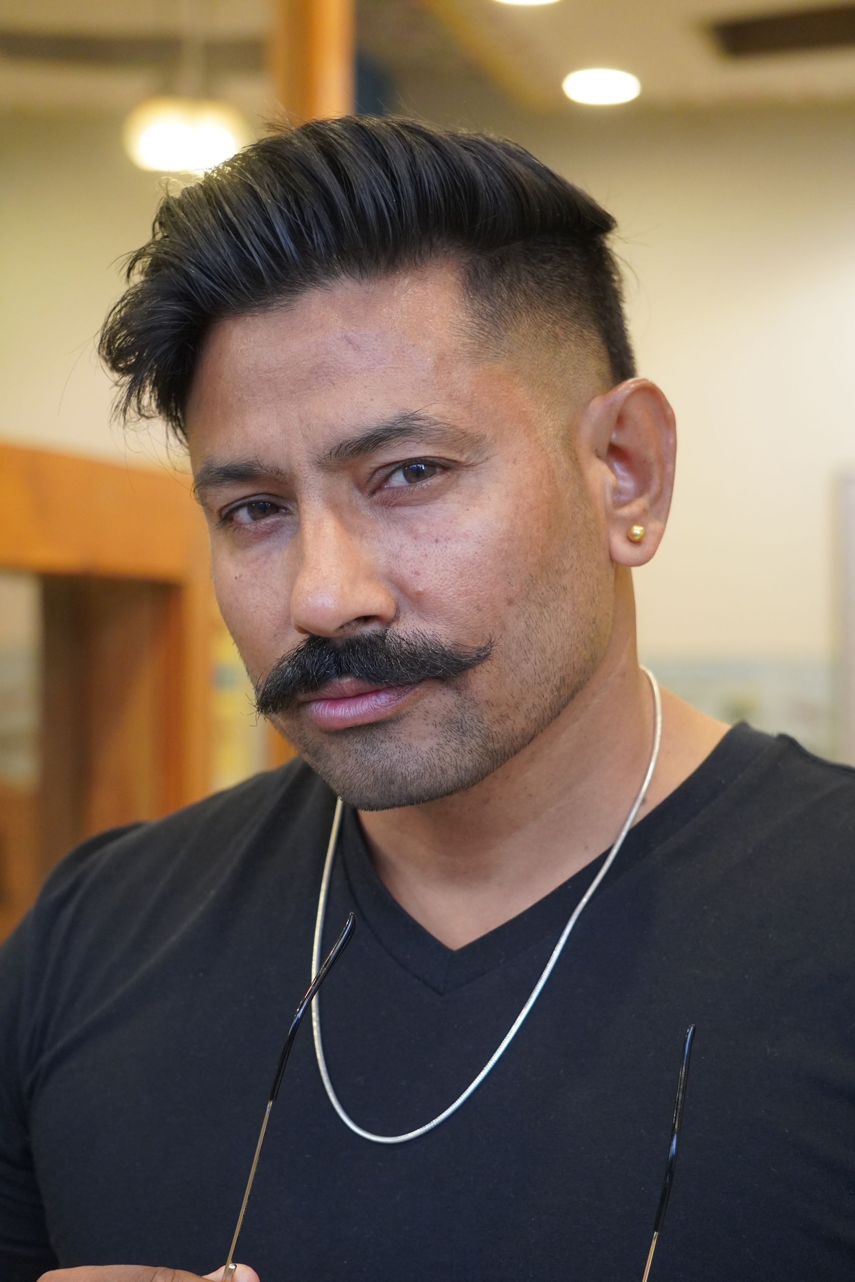Portrait of a confident man with a stylish mustache wearing a black shirt indoors.